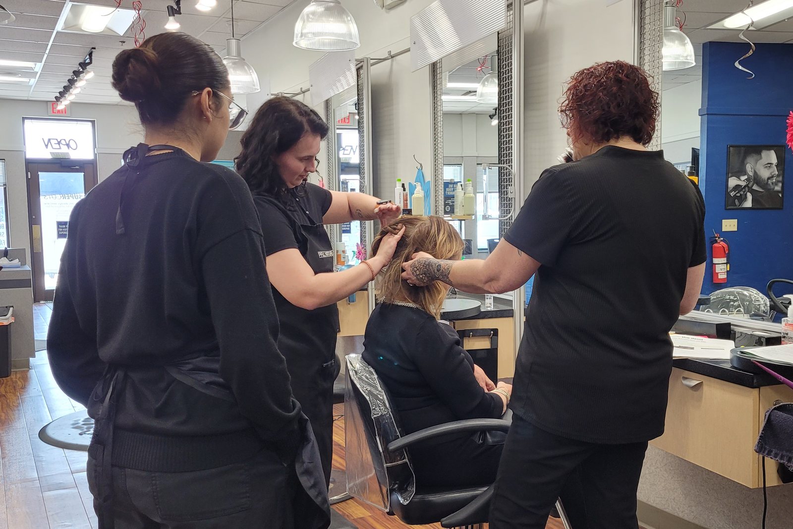 Two experienced stylists coaching at the chair in one of our salons while a newer team member watches