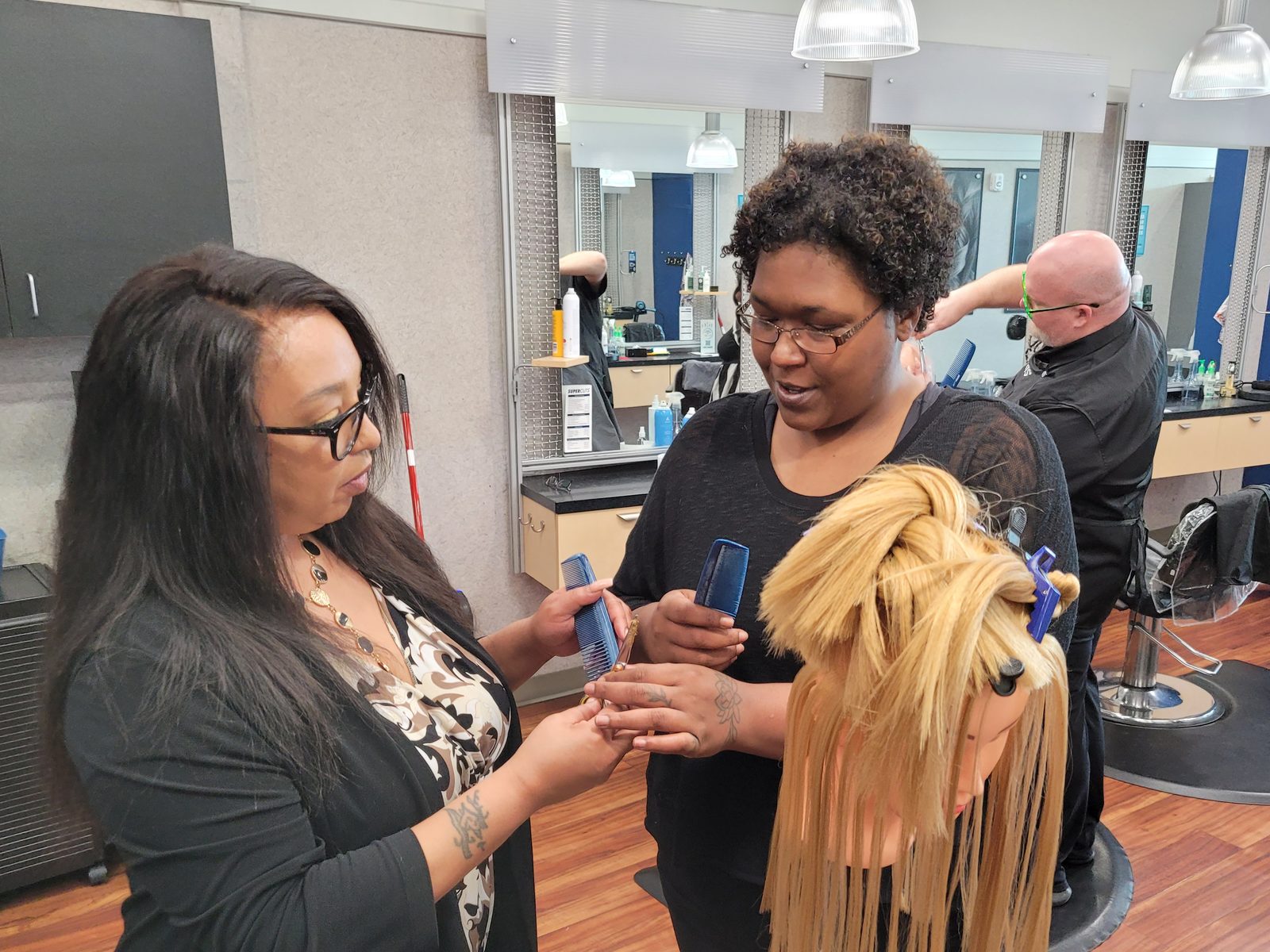 A salon manager coaching an apprentice's comb technique on a mannequin in one of our salons